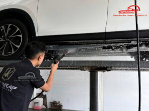 Kỹ thuật viên vệ sinh gầm xe bằng máy xịt áp lực cao.